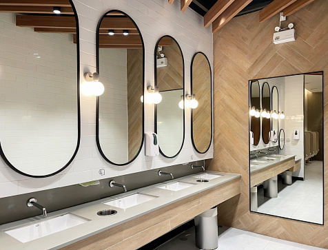 Minimal style and modern beautiful interior design of public restroom with row of mirrors, sinks with faucets, bright decorating light, ceramic wall fllor and emergency light.