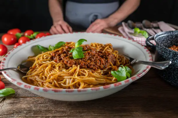 Fresh and traditional homemade cooked spaghetti with bolognese sauce. Served in a llarge past bowl with basil on rustic and wooden table background. Closeup, front