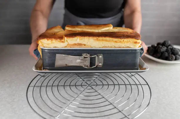 Traditional old german cheesecake fresh and homemade baked in a baking pan. Served by a woman with apron on a cooling rack. Closeup, front view