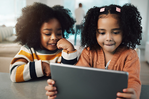Sisters, children and girls smile with tablet in home, playing games and bonding together. Technology, family and happy mixed race kids with touchscreen for elearning, streaming movie or web browsing