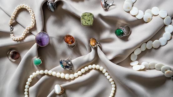 Many different silver rings and necklace with various natural gemstones over  background.