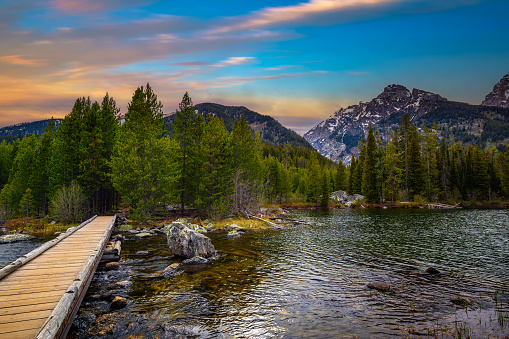 Sunset over Taggart Lake and Grand Teton Mountains in Wyoming, USA, with a footbridge in the foreground.
