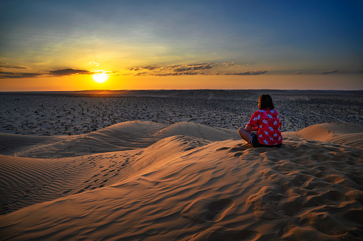 Woman watching a sunset over the sand dunes of the Arabian Desert in Oman, near the city of Salalah.