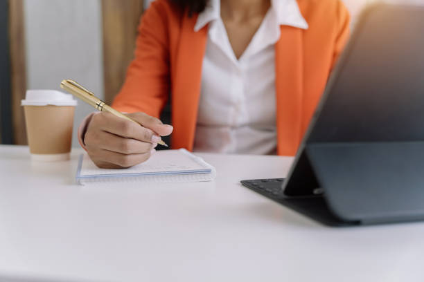 istock Business woman hand working at a tablet, computer and writing on a notepad with a pen in the office. 1495318449
