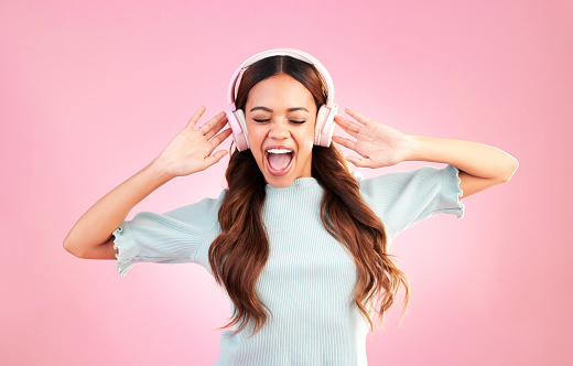 Music headphones, singing and woman dance in studio isolated on a pink background. Singer, dancing and happy mixed race female streaming, enjoying and listening to audio, sound track or radio podcast
