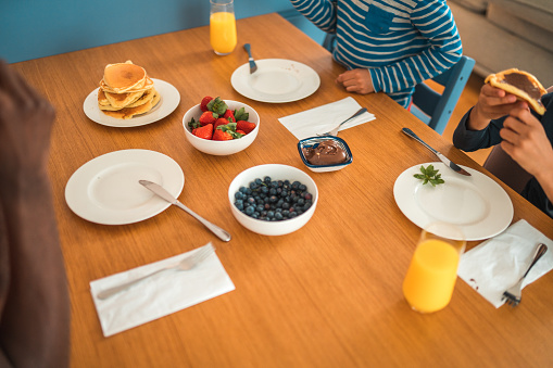 The table is adorned with stacks of fluffy American pancakes, fresh strawberries and blueberries, and refreshing juice, setting the scene for a delightful family breakfast.