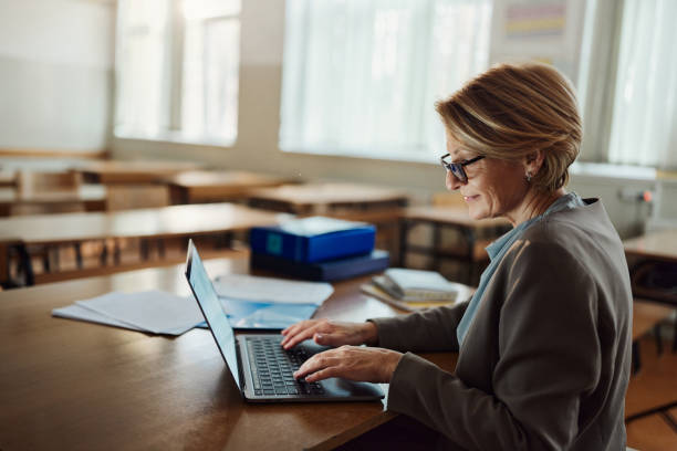 Smiling female teacher working on laptop in the classroom. - fotografia de stock