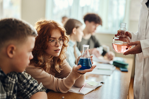 Redhead female high school student analyzing blue liquid while having a science class in the classroom.