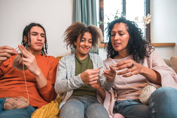 The younger generation learning old-fashioned crafty hobbies. Happy mix-raced brother and sister knitting with their mother and grandmother in a retro-style living room.