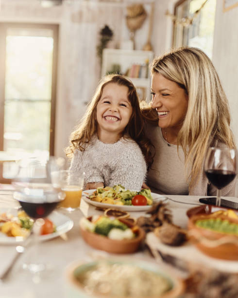 Happy mother and daughter enjoying during a meal at dining table.