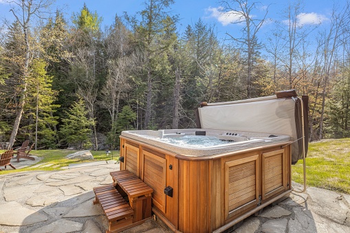 Outdoor hot tub situated on a wooden patio, surrounded by lush greenery and a wooden picnic table nearby