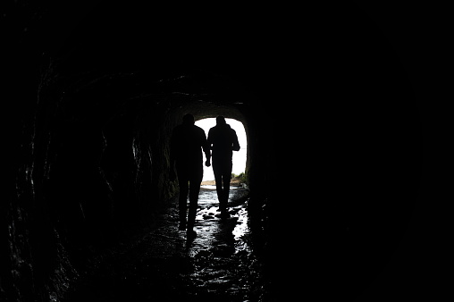 Silhouette of a man walking through a dark tunnel in a cave