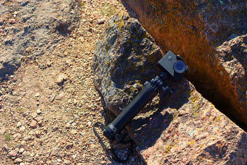 Action camera with a selfie stick lying on the rocks