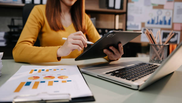 istock Business woman sitting front tablet ,laptop computer with financial graphs and statistics on monitor at office 1495328978