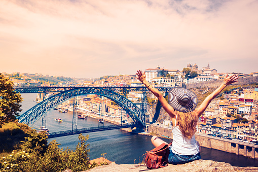 Traveler woman with arms raised enjoying panoramic view of Porto city,  old town and Douro river with famous bridge- Portugal