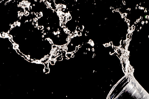 Drinking water splashing from the glass on black background