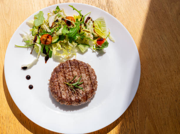 Beef cutlet grill with stripes outdoors and fresh salad on a white plate.