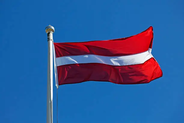 Latvian flag waving in the wind on a blue summer sky