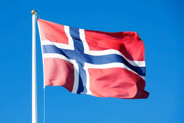 Norway's flag waves in the wind against the blue summer sky