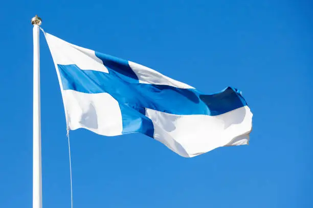 The flag of Finland waves in the wind against the blue summer sky