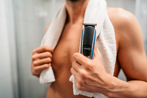 Close-up of a young man holding an electric razor in the bathroom in the morning.