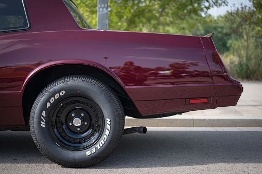 Sabadell, Spain – February 18, 2023: Detail of the rear wheel and exhaust pipe of a classic maroon usa muscle car