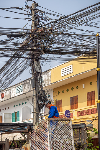 Luang Prabang, Laos - March 14th 2023: Man working on a pole with a confusing number of cables in the center of the former capital of Laos