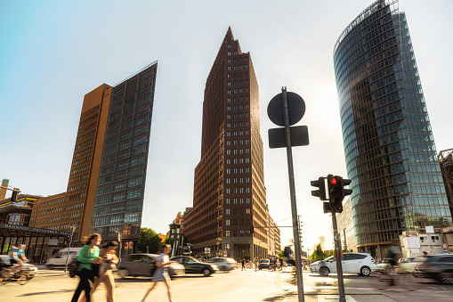 motion blurred people and cars crossing street at potsdamer platz in berlin in the backlit of afternoon sun