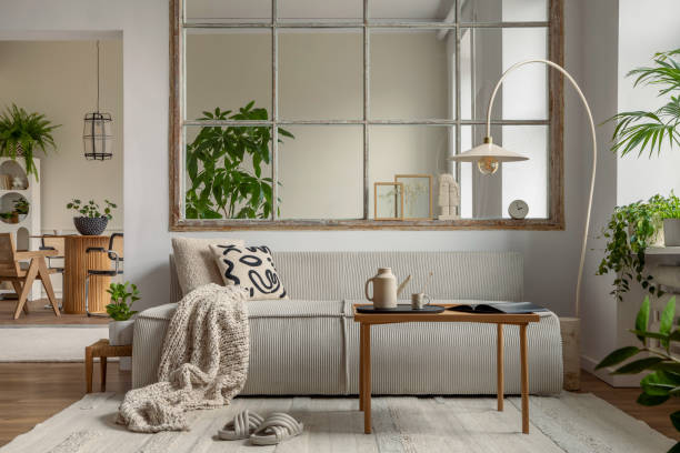 istock Interior design of open space interior with modular sofa, big window, stylish lamp, wooden coffee table, round table, rattan chair, pillows, plants and personal accessories. Home decor. Template. 1495354613