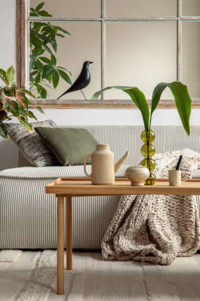 istock Aesthetics composition of open space interior with modular sofa, wooden coffee table, beige pitcher, window, braided plaid, glass vase with leaves and personal accessories. Home decor. Template. 1495354656
