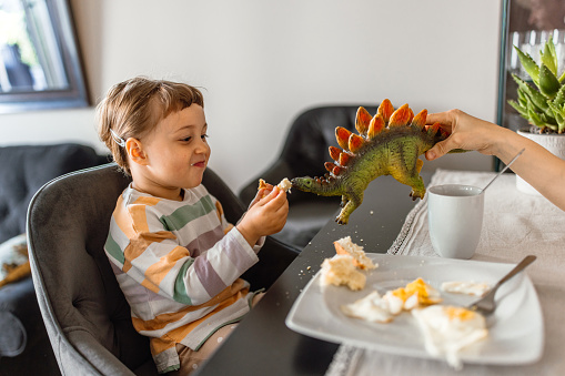 Cute little girl having a breakfast in the morning. Little girl pretending to feeding a dinosaur toy, while eating egg breakfast.