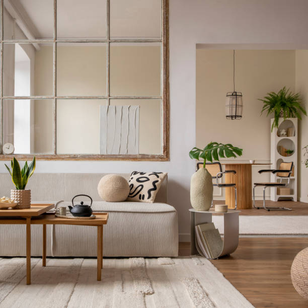 istock Creative composition of living room interior with modular sofa, beige rug, plants, vase with green leaves, pouf, stylish coffee table, big window, lamp and personal accessories. Home decor. Template. 1495354724