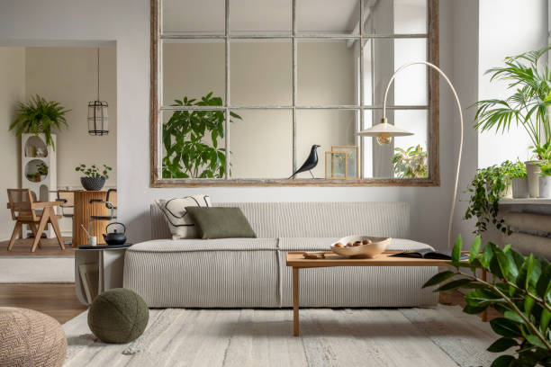 istock Interior design of open space interior with modular sofa, big window, stylish lamp, wooden coffee table, round table, rattan chair, pillows, plants and personal accessories. Home decor. Template. 1495354730