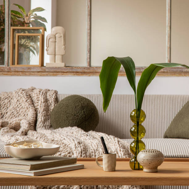 Aesthetics composition of open space interior with modular sofa, wooden coffee table, cup window, braided plaid, books, bowl, glass vase with leaves and personal accessories. Home decor. Template.