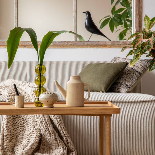istock Aesthetics composition of open space interior with modular sofa, wooden coffee table, beige pitcher, window, braided plaid, glass vase with leaves and personal accessories. Home decor. Template. 1495354793