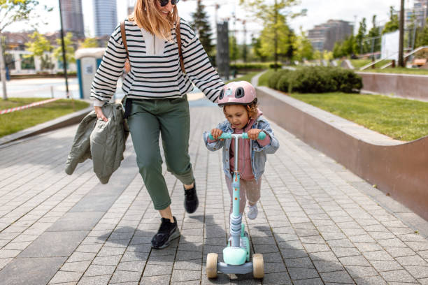 istock Mother and daughter having fun with push scooter in public park 1495357475