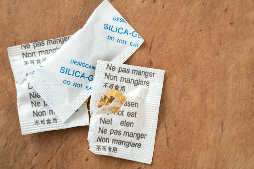 silica gels, closeup of silica gel packages with cautions in different languages. granular balls for absorbing moist or humidity. small yellow silicate balls with selective focus. package with caution