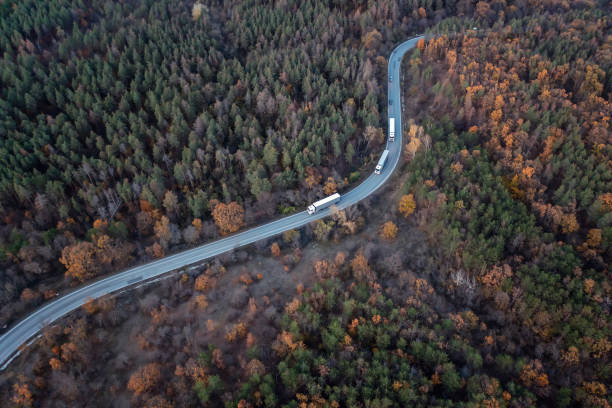 Aerial view above a colorful autumn forest with a curved country road with large trucks