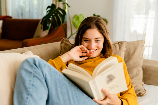 Young woman relaxing on sofa at home and reading book