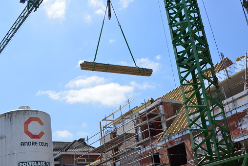 Wilsele, Vlaams-Brabant, Belgium - June 2, 2023: construction crane transports a heap of pine wood planks from the ground floor upwards, which will serve for the construction of the roof