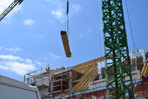 Wilsele, Vlaams-Brabant, Belgium - June 2, 2023: construction crane transports a heap of pine wood planks from the ground floor upwards, which will serve for the construction of the roof
