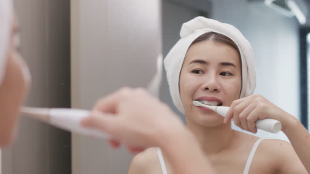 Beautiful Asian Woman Brushing Teeth Near Mirror In Bathroom