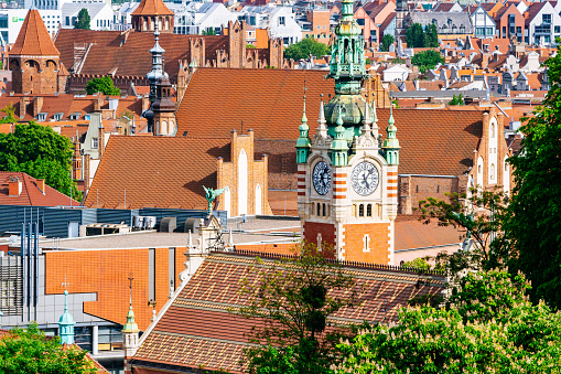 Zoomed-in perspective of Gdansk's Old Town as seen from Gradowa Hill. The focal point of the composition is the Clock Tower of Gdansk Main Station (Gdańsk Główny), standing prominently in the center of the frame. Surrounding the tower, numerous old buildings with vibrant red roofs fill the scene, showcasing the architectural charm of the historic district. This close-up view provides a detailed glimpse of the unique rooftops that define Gdansk's Old Town.