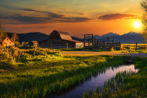Colorful sunset over Historic John Moulton Barn at Mormon Row in Grand Teton National Park on a sunny summer day, with Teton Mountain Range in the background.