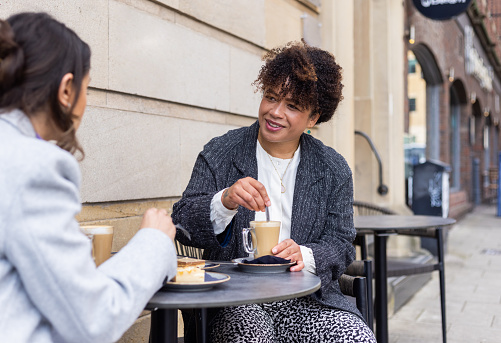 Two businesswomen sitting down outside and holding a meeting over coffee.  They are wearing smart casual business clothing.