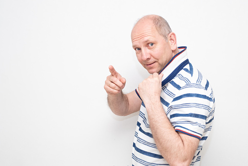 A Caucasian man 50 years old on a gray background in a light shirt smiles and points with his hand in the direction. series of emotions.