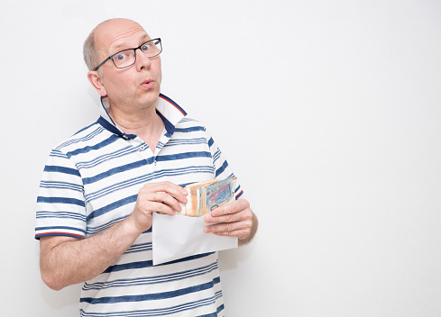 A Caucasian man 50 years old on a gray background in a light shirt takes out a pack of euro bills from an envelope and whistled. series of emotions.
