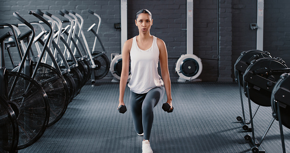 Woman, portrait and fitness with dumbbells in lunges for workout, exercise or training at the gym. Fit, active and sporty female person in split squat or lunge with weights for healthy exercising