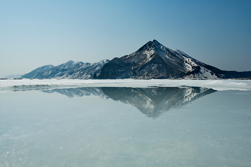 Russia. Far East, Sakhalin Island. View of an extinct volcano surrounded by spring ice on the shore of the Tikhaya Bay of the Gulf of Patience in the Sea of Okhotsk.