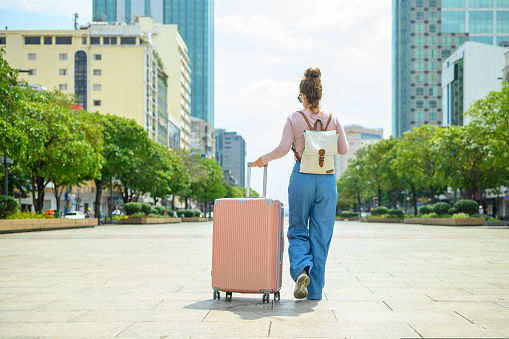 Unrecognizable woman with suitcase and backpack walking along city street